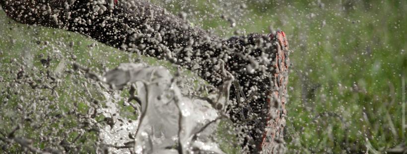 Stock photo of a leg running through a muddy puddle. The mud is splashing up towards the camera.
