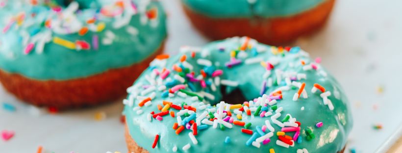 Photo of a tray of ring doughnuts. They have green icing and multicoloured sprinkles.